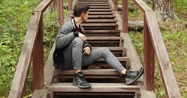 Young man sitting on stairs in forest - Footage, Video