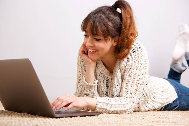 Portret van de jonge vrouw liggend op de vloer met laptopcomputer - Foto, afbeelding