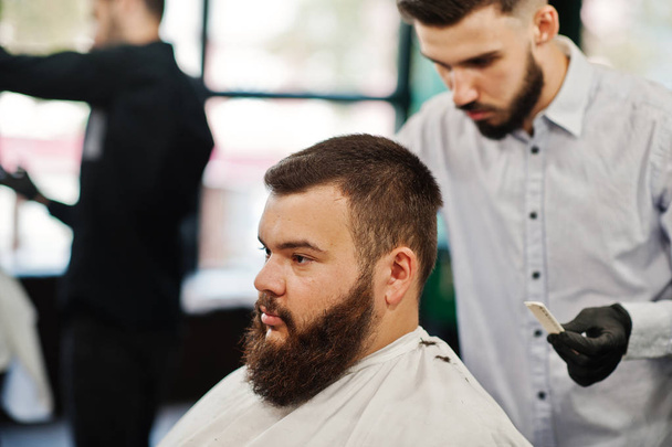 Handsome bearded man at the barbershop, barber at work. - Фото, изображение