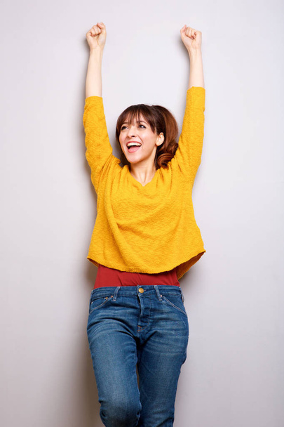 Muotokuva onnellinen nuori nainen nauraa kädet kohotetaan harmaata taustaa vasten
 - Valokuva, kuva