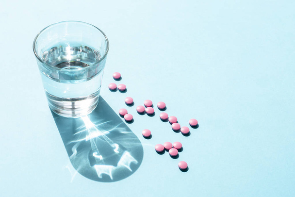 Вода в скляних Кубок і рожевий круглі таблеток на синій поверхні - Фото, зображення
