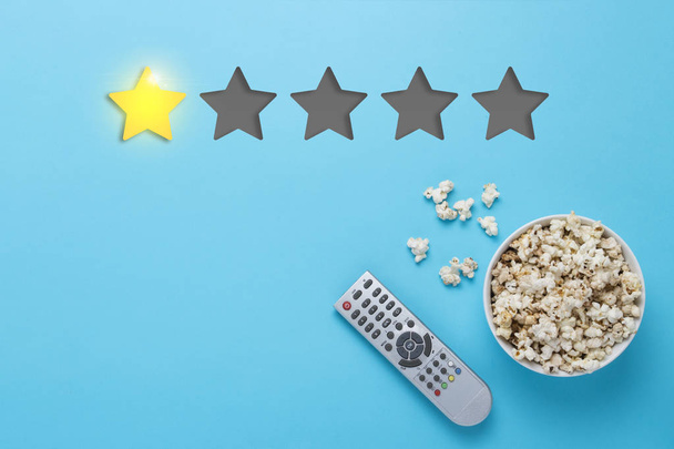 Bowl of popcorn and a remote from the TV set on a blue background. Rating one star out of five. Concept of the rating of the film, TV series, TV show. Flat lay, top view. - Photo, Image