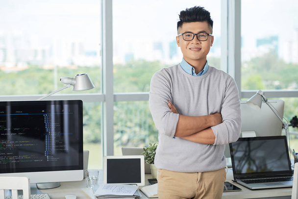 Портрет молодого бизнесмена в очках, стоящего в современном ИТ-офисе
 - Фото, изображение