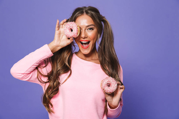 Portrait of a cute girl in sweatshirt posing with donuts isolated over violet background - Fotó, kép