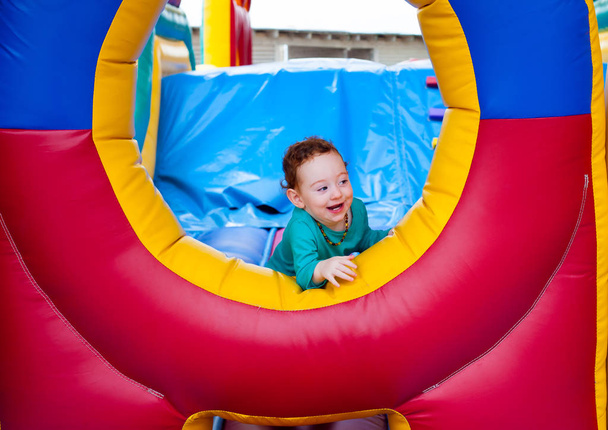Περίεργος αστεία μικρό παιδί κρυφοκοιτάζει έξω από το πολύχρωμο τραμπολίνο κάστρο - Φωτογραφία, εικόνα