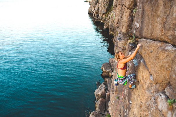 水の上のクライマー。女性は、岩を登っていきます。自然の地形でのトレーニング。極端なスポーツ。海岸沿いに登山ルート. - 写真・画像