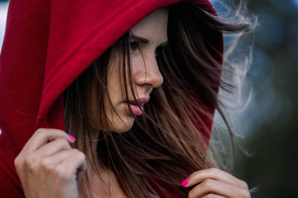 Closeup portrait of beautiful young woman wearing red swimsuit and red hoodie, blurred background - Фото, изображение