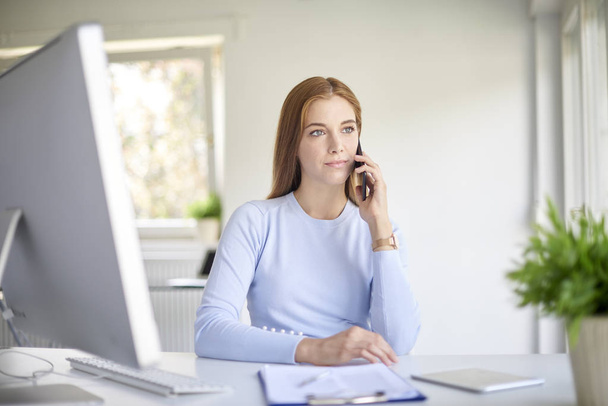 young sales assistant businesswoman using her mobile phone sitting at desk in office.  - Foto, imagen