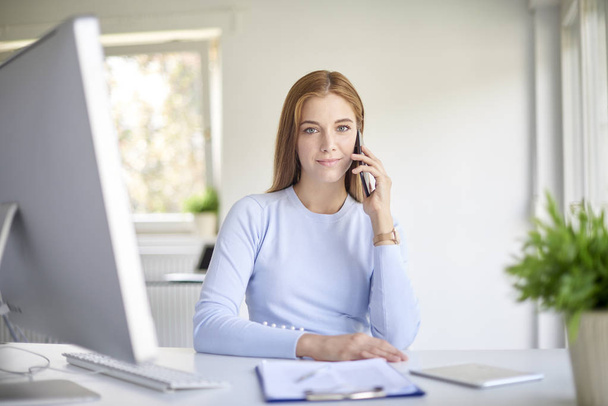 young sales assistant businesswoman using her mobile phone sitting at desk in office.  - Foto, Bild