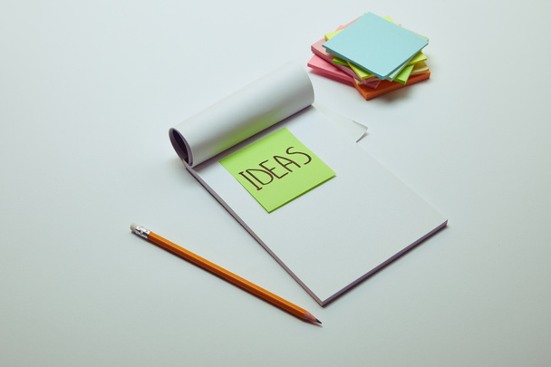 paper sticker with word ideas in notebook, pencil and pile of note papers on white tabletop - Fotografie, Obrázek