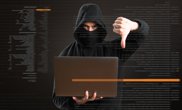 Hacker con su ordenador haciendo mala señal en el fondo oscuro
 - Foto, imagen