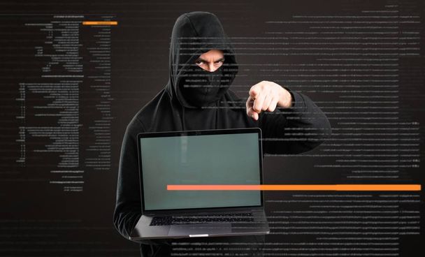 Hacker zijn computer wijzend naar het front op donkere achtergrond - Foto, afbeelding