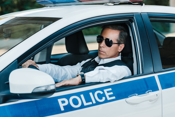 confident mature policeman in sunglasses sitting in car  - Fotografie, Obrázek
