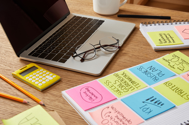papieren stickers met de bedrijfsstrategie, rekenmachine en laptop op tafelblad - Foto, afbeelding