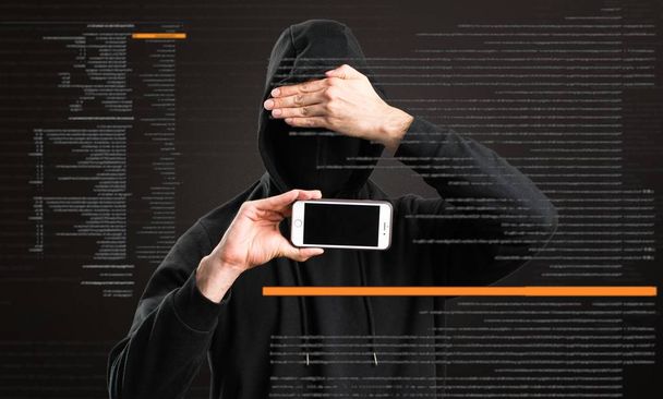 Hacker met zijn mobiele die betrekking hebben op zijn gezicht op donkere achtergrond - Foto, afbeelding