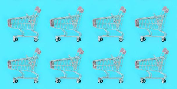 Einkaufssucht, Shopping-Liebhaber oder Shopaholic-Konzept. viele kleine leere Einkaufswagen führen ein Muster auf pastellfarbenem Papierhintergrund aus. flache Verlegekomposition, Ansicht von oben - Foto, Bild