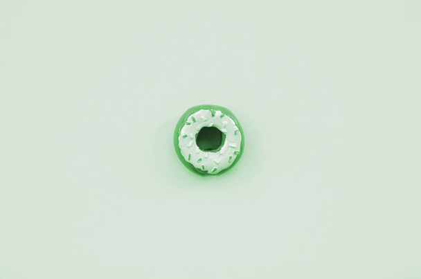 Ein einzelner kleiner Kunststoff-Donut liegt auf einem pastellfarbenen Hintergrund. flach lag minimale Zusammensetzung. Ansicht von oben - Foto, Bild