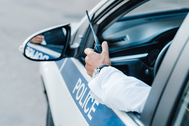 imagem cortada de policial masculino segurando rádio definido no carro
  - Foto, Imagem