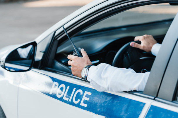 cropped image  of male police officer holding walkie-talkie in car  - Fotografie, Obrázek