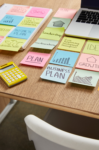 papieren stickers met de bedrijfsstrategie, rekenmachine en laptop op tafel - Foto, afbeelding