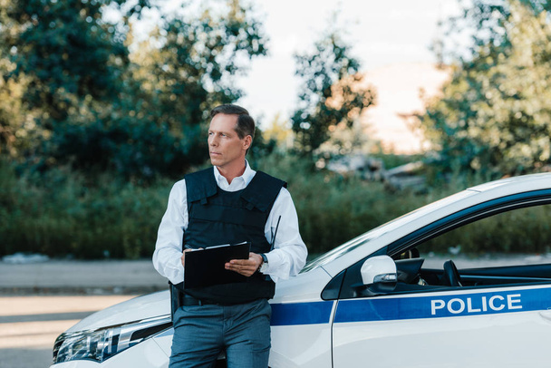 středního věku muže policista neprůstřelnou vestu, psaní do schránky u auta na ulici  - Fotografie, Obrázek