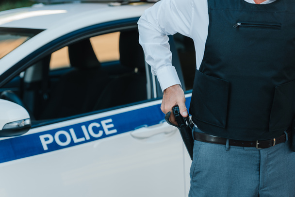 cropped image of policeman in bulletproof vest taking off gun from holster near car at street - Fotoğraf, Görsel