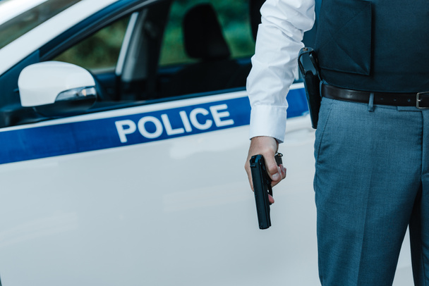 cropped image of policeman in bulletproof vest holding gun near car at street - Fotografie, Obrázek