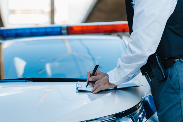 imagem cortada de policial masculino escrevendo na área de transferência no carro na rua
 - Foto, Imagem