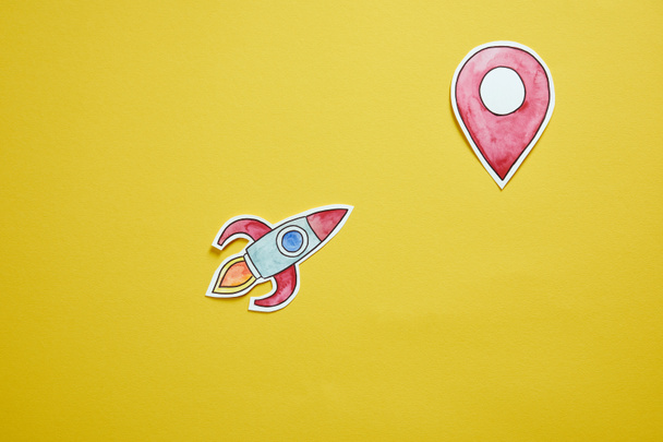 top view of paper rocket and location sign isolated on yellow - Photo, Image