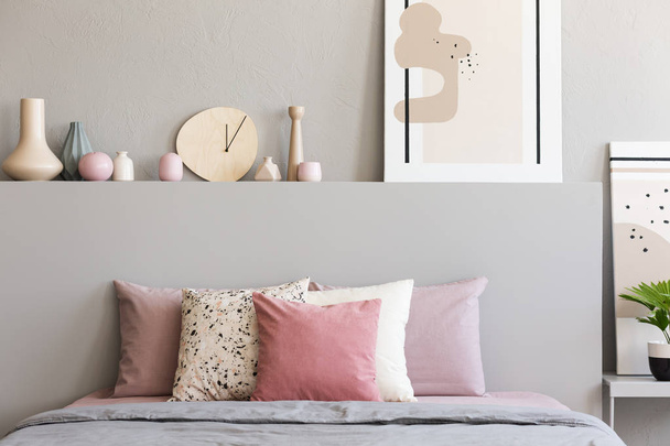 Pink and white pillows on grey bed in pastel bedroom interior with poster on bedhead. Real photo - Фото, изображение