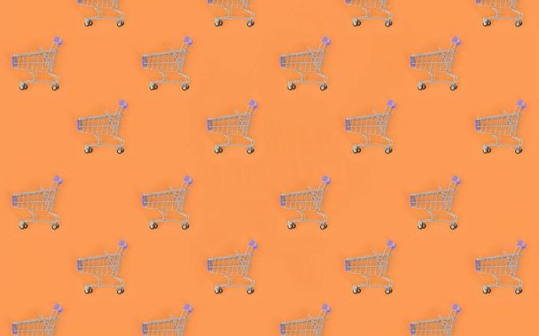 Shopping addiction, shopping lover or shopaholic concept. Many small empty shopping carts perform a pattern on a pastel colored paper background. Flat lay composition, top view - Photo, Image
