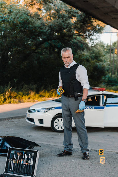 Koncentrovaná muž policista v latexových rukavic na místo činu s mrtvolou v pytli  - Fotografie, Obrázek