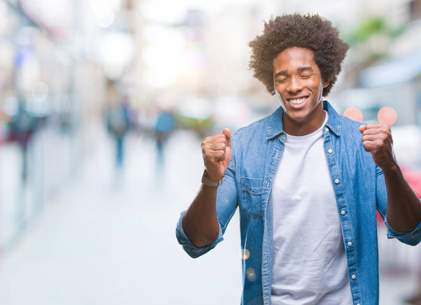 Afro americký muž nadšený pro úspěch s náručí izolované pozadí aktivována, oslavující vítězství úsměv. Vítěz koncept. - Fotografie, Obrázek