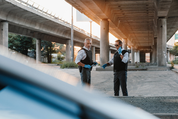 policial masculino em colete à prova de balas de pé perto colega enquanto ele fala no rádio set na rua da cidade
 - Foto, Imagem