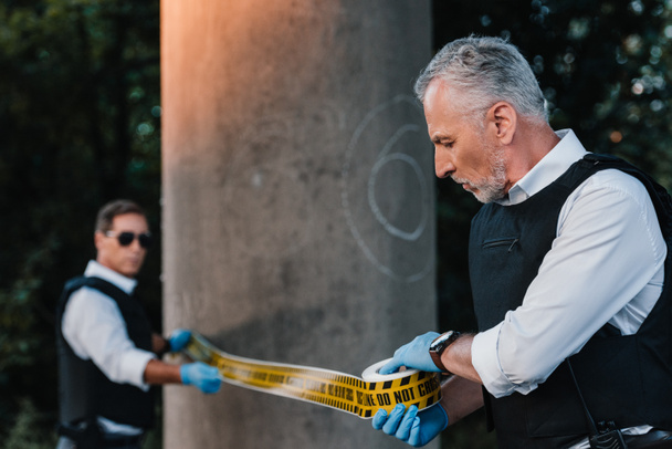 ラテックスの成熟した男性警察官のセレクティブ フォーカス手袋犯行現場で警察ラインを設定  - 写真・画像