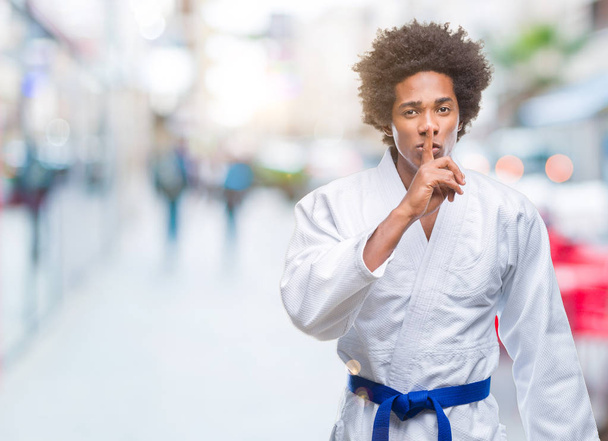 Afro amerikkalainen mies yllään karate kimono yli eristetty tausta pyytää olla hiljaa sormi huulilla. Hiljaisuus ja salainen käsite
. - Valokuva, kuva
