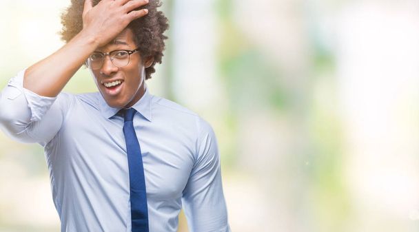 Afro Amerikaanse zakenman dragen bril over geïsoleerde achtergrond verrast met hand op hoofd voor fout, niet vergeten fout. Vergat, slecht geheugen concept. - Foto, afbeelding