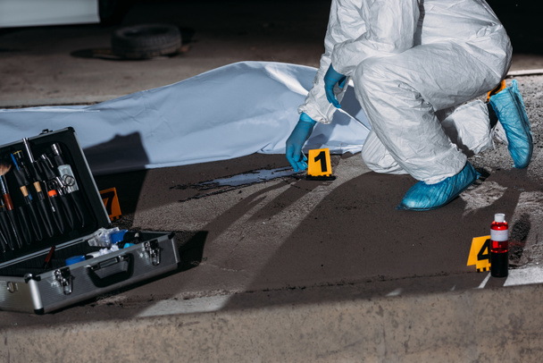 cropped image of criminologist in protective suit and latex gloves collecting evidence at crime scene with corpse  - Foto, afbeelding