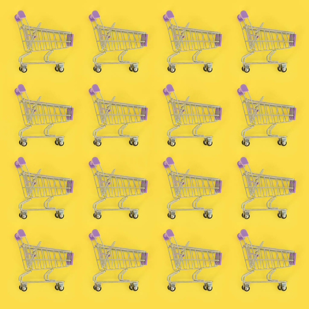 Vício em compras, amante de compras ou conceito shopaholic. Muitos pequenos carrinhos de compras vazios executam um padrão em um fundo de papel colorido pastel. Composição de leigos planos, vista superior
 - Foto, Imagem