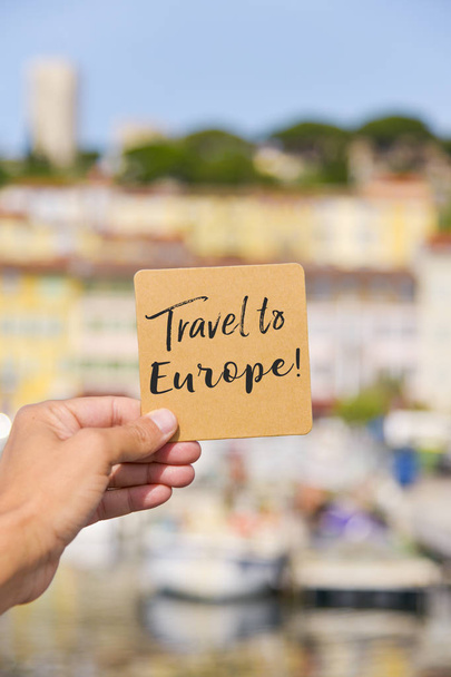 un jeune caucasien tenant une pancarte brune avec le texte voyage vers l'Europe écrit en elle, dans le Vieux Port, le Vieux Port de Cannes, France, avec Le Suquet, la vieille ville, en arrière-plan
 - Photo, image