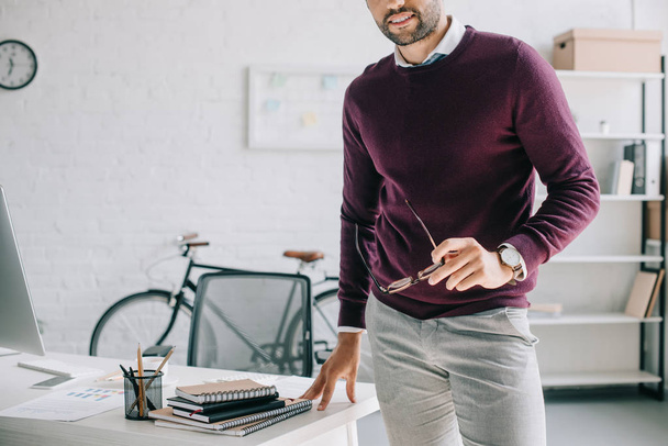 imagen recortada de hombre de negocios sonriente en jersey de color burdeos con gafas en la oficina
 - Foto, imagen