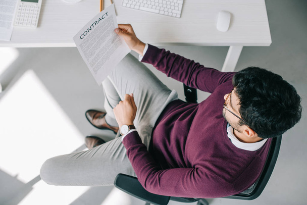 високий кут зору дизайнера в бордовому светрі читання контракту в офісі
  - Фото, зображення