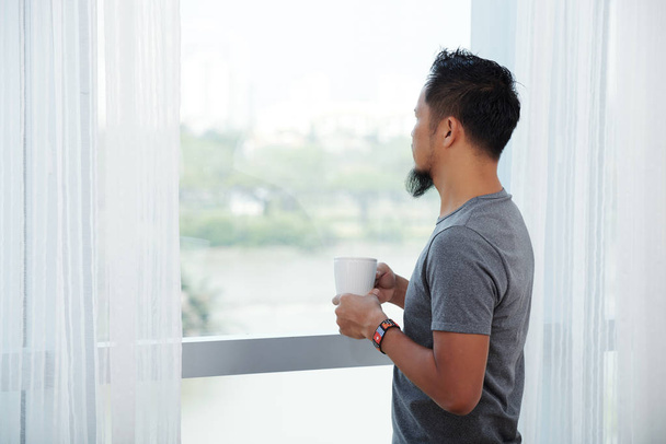 Uomo che beve il suo caffè del mattino e guarda attraverso la finestra
 - Foto, immagini