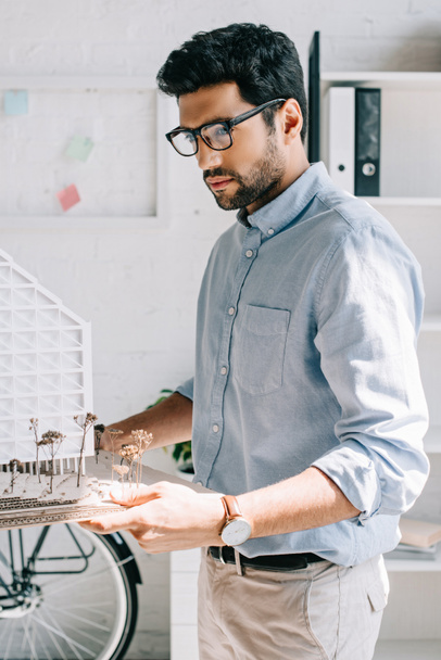 side view of handsome architect holding architecture model in office - Foto, Bild
