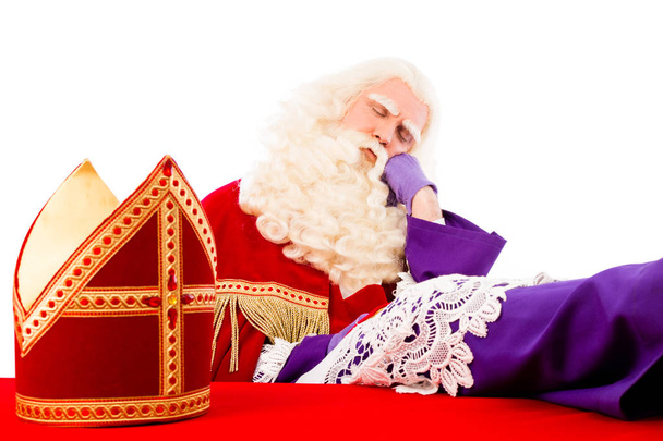 Der Heilige Nikolaus mit Mitra auf dem Tisch ist müde und schläft. isoliert auf weißem Hintergrund - Foto, Bild