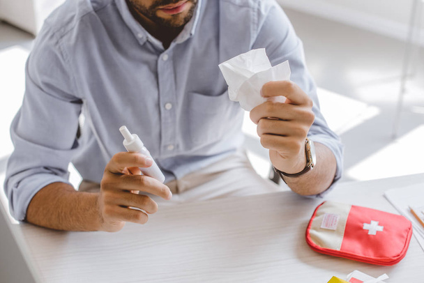 cropped image of sick manager holding nasal spray and tissue in office - Photo, Image