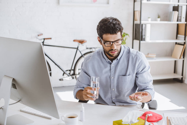 sick manager holding pills and glass of water at table in office - Photo, Image
