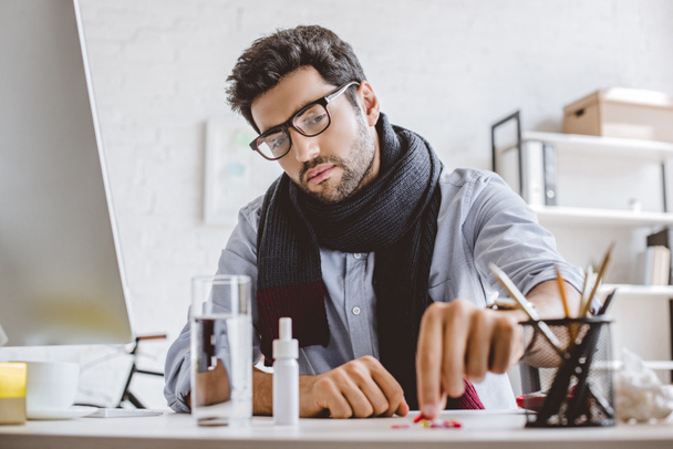 sick businessman in scarf taking pill from pile in office - Photo, Image