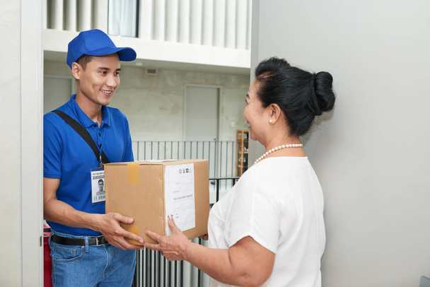 Cheerful Asian courier giving big box to aged woman - Foto, Imagen