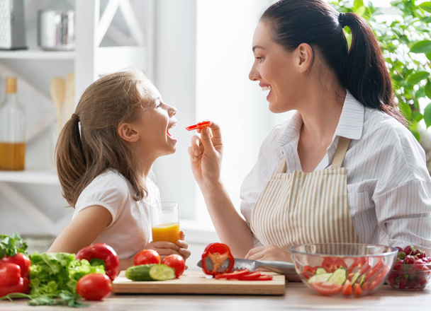 Healthy food at home. Happy family in the kitchen. Mother and child daughter are preparing the vegetables. - Valokuva, kuva